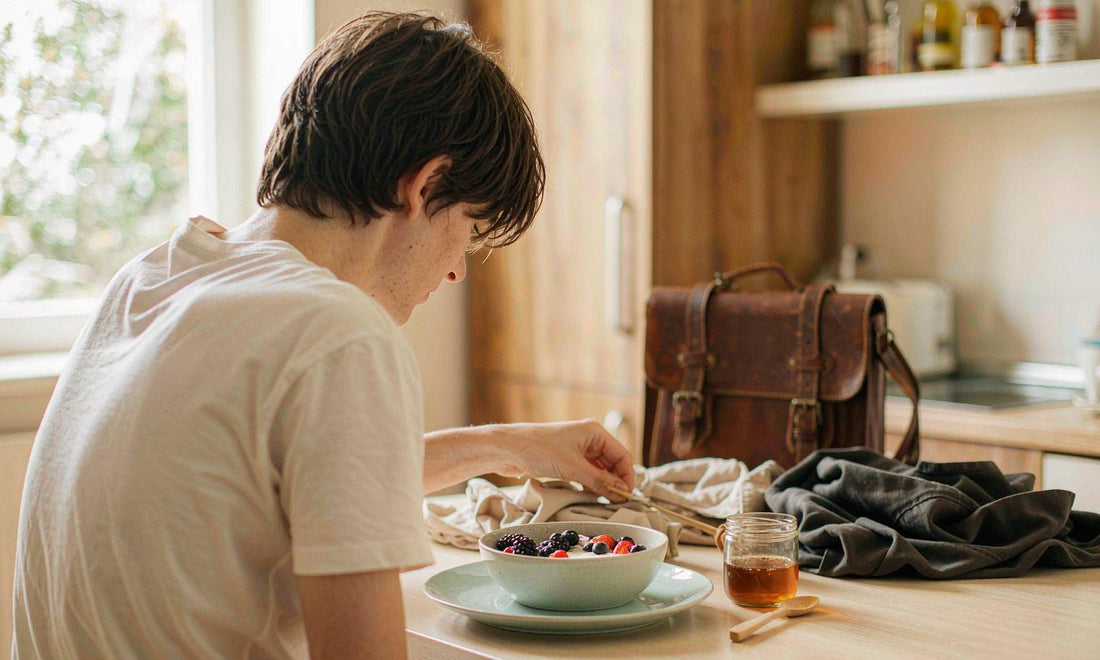 Breakfast laid out at a sunlit table with yogurt and berries beside a waiting school bag