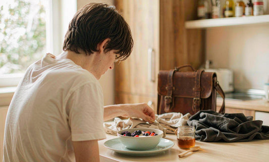 Breakfast laid out at a sunlit table with yogurt and berries beside a waiting school bag