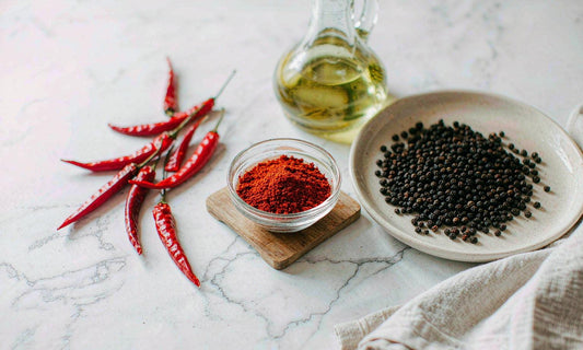 Ingredient flat lay of dried cayenne peppers, ground red spice, black peppercorns and olive oil on marble