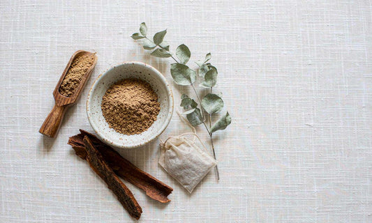 A bowl of fine tan bark powder with dried bark strips and a linen tea bag on pale cloth