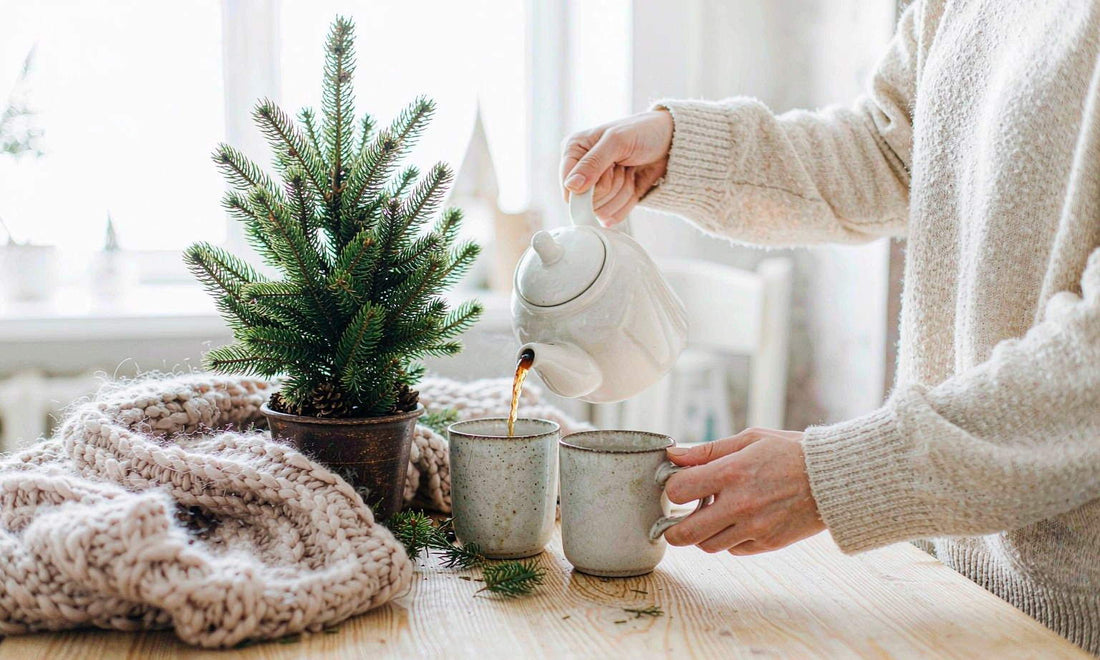 Warm winter family scene: tea poured into two stoneware mugs on a light oak table