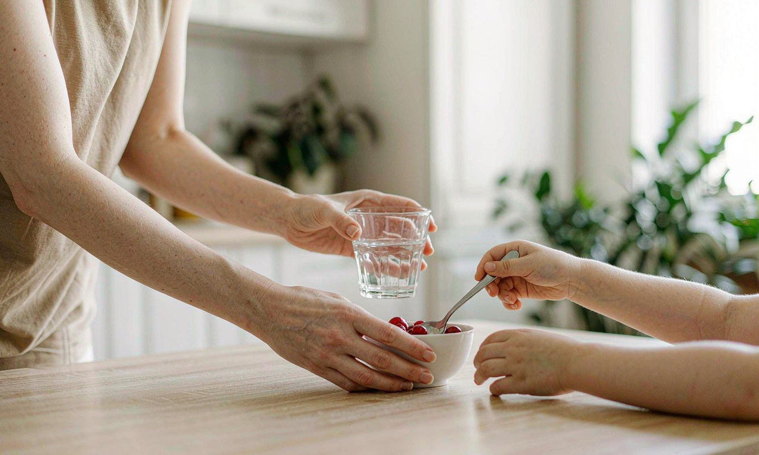 Sunlit breakfast table with a woman's hands setting water and berries beside a child's hand
