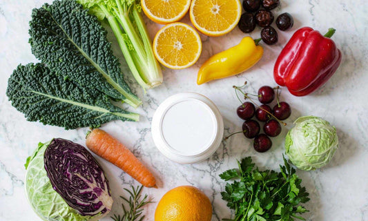 Supplement jar surrounded by colorful vegetables, citrus and leafy greens on a bright white marble counter