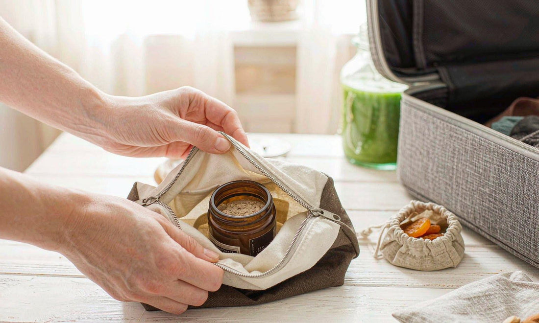 A traveler's hands packing an amber supplement jar into a canvas pouch beside dried fruit and a suitcase
