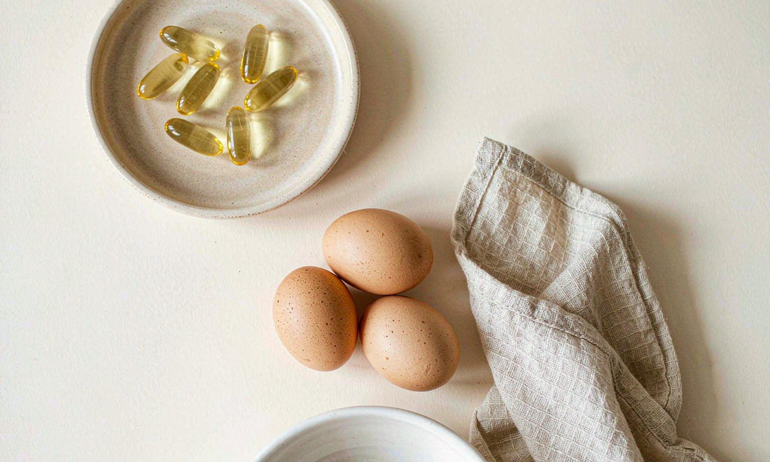 Golden softgel capsules arranged on a pale ceramic dish with eggs and linen at a bright breakfast table