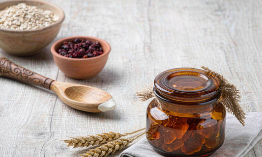An amber jar of whole-food gummies surrounded by rustic pantry staples and grains on a white oak table