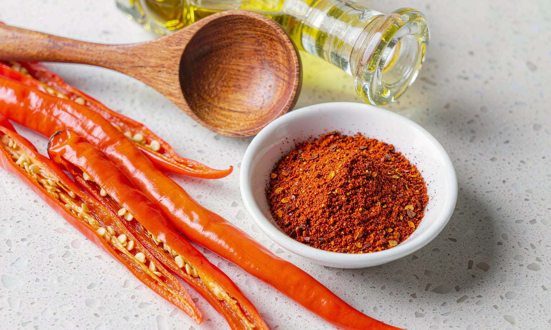 Flat lay of dried cayenne peppers, ground red spice and a wooden spoon on a light stone countertop