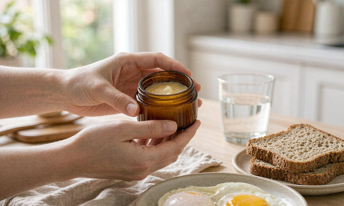 Hands holding a small unlabelled amber jar beside a plate of eggs and wholegrain toast at breakfast