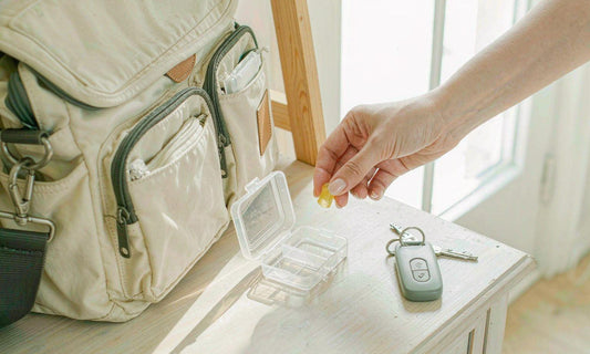 A hand placing a gummy into a small travel pill case beside a canvas commuter bag on an entryway table