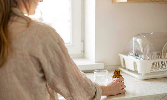 Bright kitchen counter with a hand reaching for a supplement bottle beside water