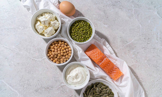 Flat-lay of eggs, lentils, chickpeas, salmon and yogurt in white dishes on pale marble