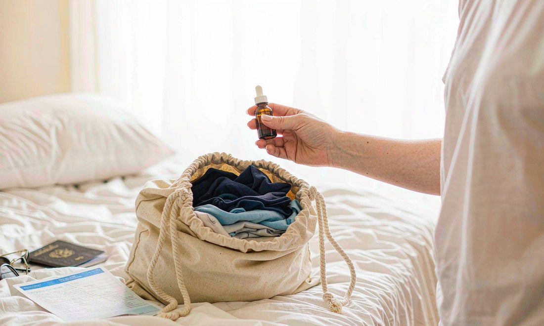 Hands packing a canvas carry-on pouch with a dropper bottle and passport on a bright hotel bed