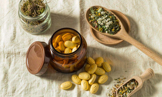 An open amber jar of golden gummy vitamins on cream linen with dried herbs and a wooden spoon