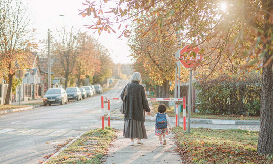Grandmother holding a childs hand walking toward school on a bright autumn morning sidewalk