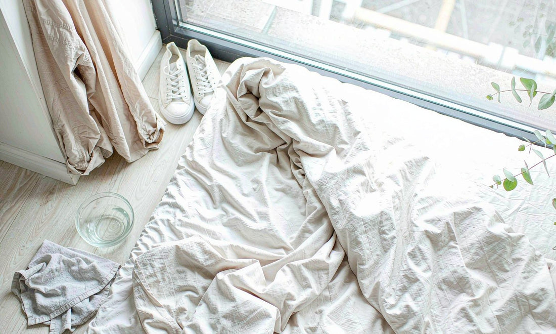 Spring reset flat-lay with folded linen bedding, sneakers and a water bowl by a bright window