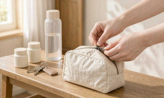 Fair-skinned hands zipping a canvas travel pouch beside two supplement jars and a water bottle on an entryway bench