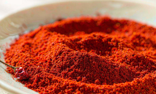 Macro of fine red cayenne powder heaped on a pale ceramic plate beside one dried chilli