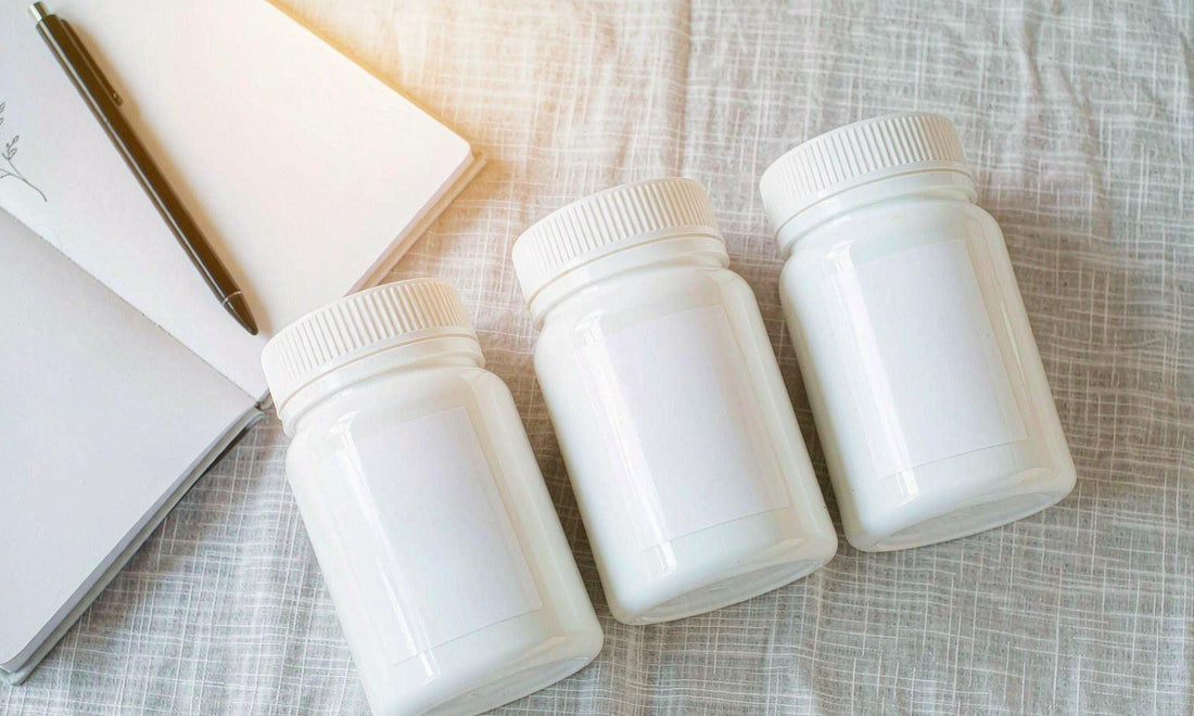 Three plain white supplement jars in a row on pale linen beside an open notebook and pen