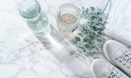 Flat-lay on white marble of a jar of pale gummies beside a water carafe, eucalyptus and walking shoes