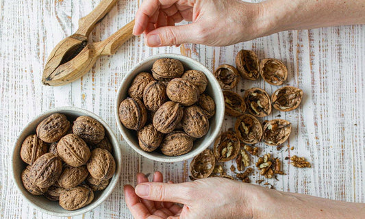 Two bowls of walnuts and a wooden nutcracker on a bright table with hands reaching from both sides