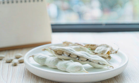 Macro view of fuzzy velvet bean pods and glossy seeds in a white ceramic dish on a pale wooden desk