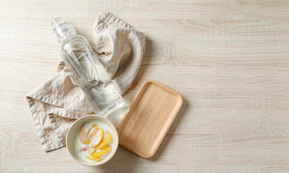 A calm family morning flat-lay with water bottle, yogurt and fruit on a pale oak table