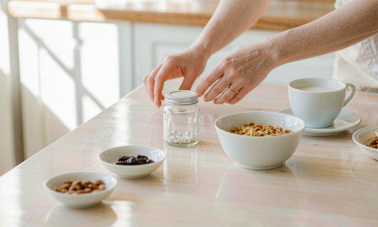 A woman's hands reaching for a supplement jar on a bright family breakfast counter in morning light
