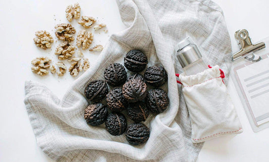 Whole black walnuts in dark shells on linen beside a canvas pouch, water bottle and a luggage tag