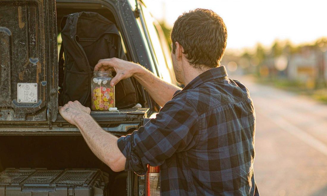 Back view of a worker in a flannel shirt packing a lunchbox and gummy jar into a work truck at sunrise