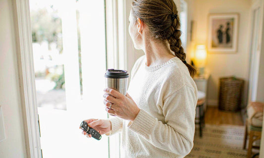 A woman in her thirties holding a travel coffee cup and car keys at a bright open front door