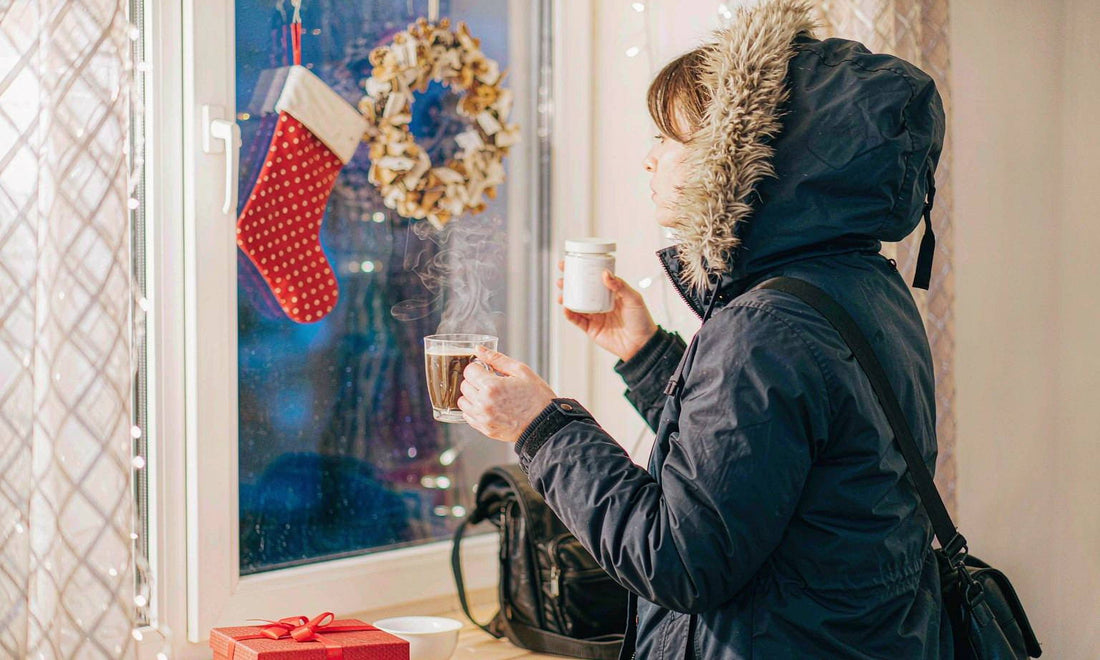 A shift worker seen from behind holding a supplement jar at a festively lit window with steam rising