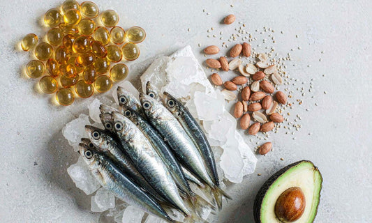 Ingredient flat lay of golden softgels, sardines on ice, raw peanuts, sesame seeds and half an avocado