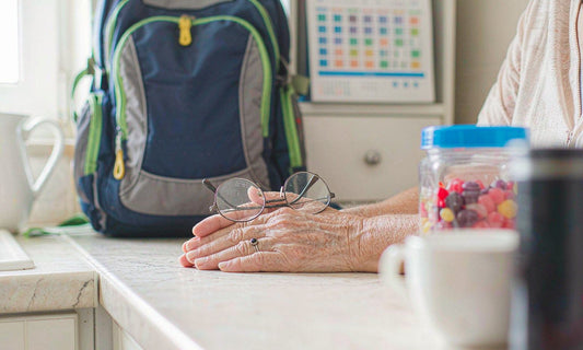 A grandmother's hands resting on a bright kitchen counter with reading glasses and a closed gummy jar