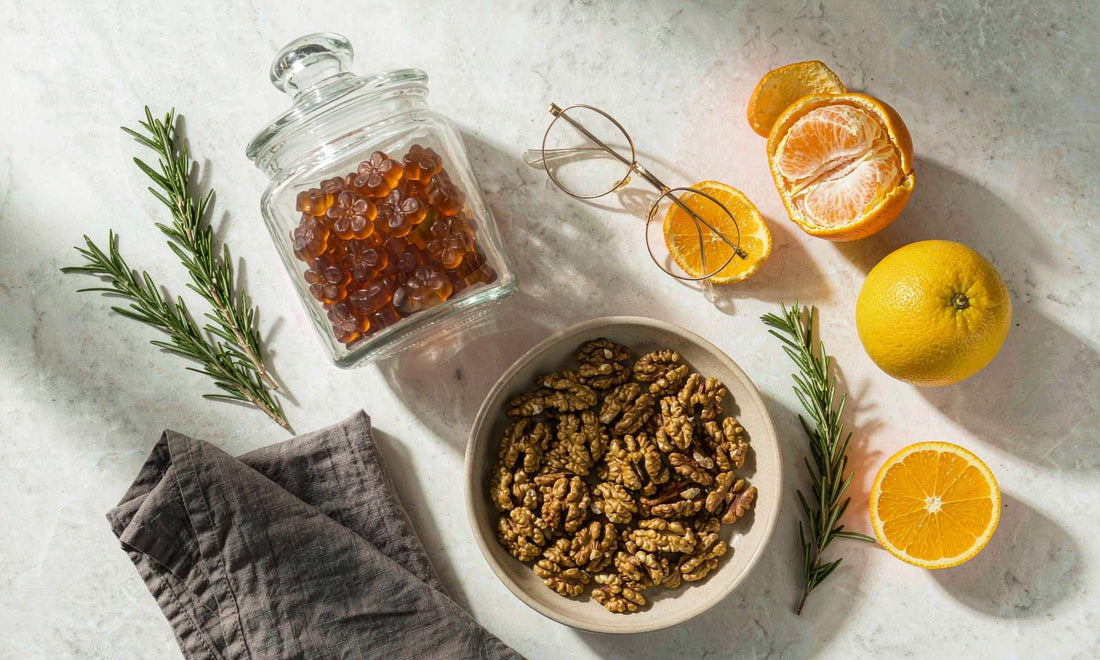 Pantry flat lay of a gummy jar, rosemary, citrus, walnuts and reading glasses on white marble