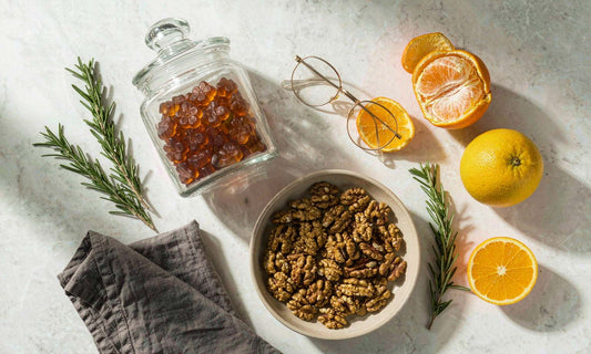 Pantry flat lay of a gummy jar, rosemary, citrus, walnuts and reading glasses on white marble