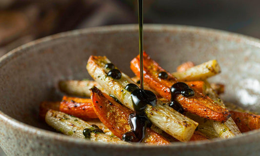 Dark green seed oil poured in a thin ribbon over roasted carrot and parsnip in a ceramic bowl