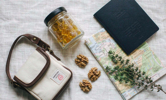 Ingredient flat lay of a gummy jar, canvas travel pouch, passport, map, walnuts and thyme on white linen