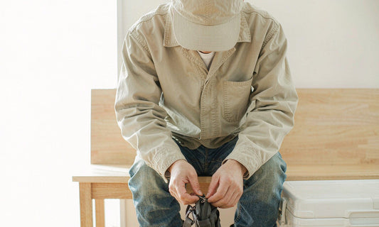 Worker in canvas jacket and cap packing a travel pouch by a bright window before a jobsite trip