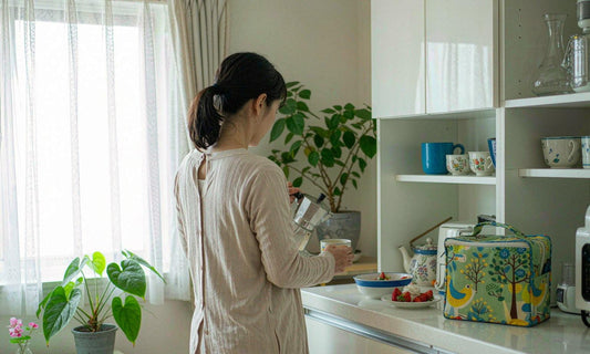 A woman in her forties pours morning coffee in a bright family kitchen with lunch bags on the counter