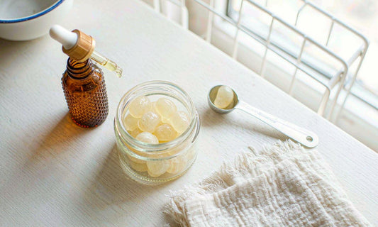 Top-down flat-lay of a gummy jar beside an amber dropper bottle and a measuring spoon on a white kitchen table
