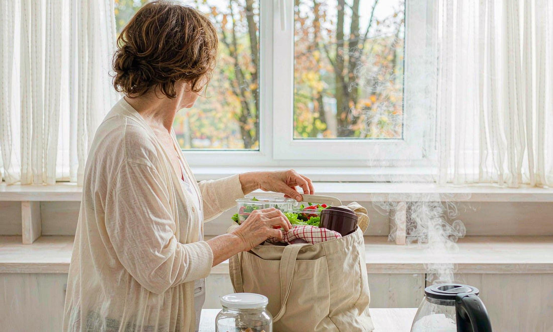 A woman seen from behind packing a school lunch bag in a bright autumn kitchen beside a gummy jar