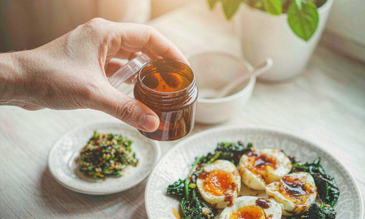 A hand holding an amber gummy jar above a plated meal of eggs and greens on a light kitchen table