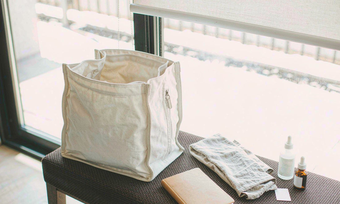 Canvas tote by a sunlit window with a dropper bottle, supplement bottle and notebook