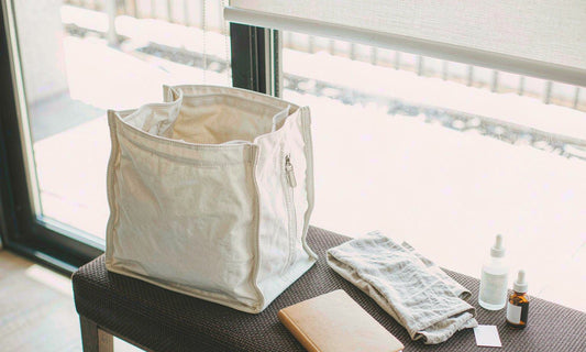 Canvas tote by a sunlit window with a dropper bottle, supplement bottle and notebook