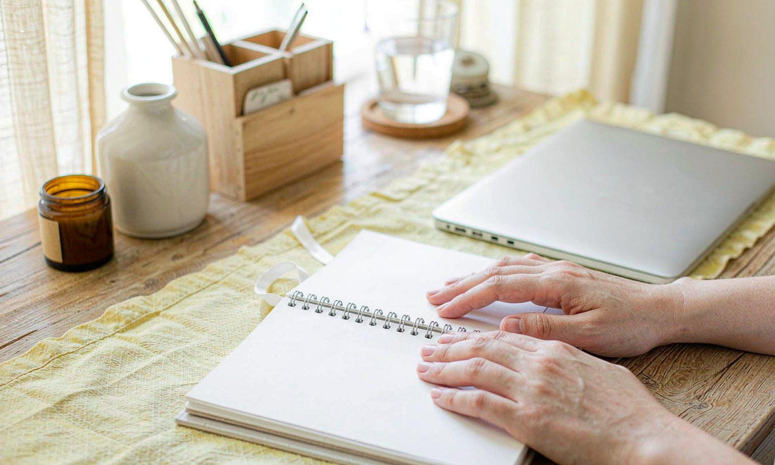 Hands resting on an open weekly planner beside a closed laptop, a water glass and an amber jar