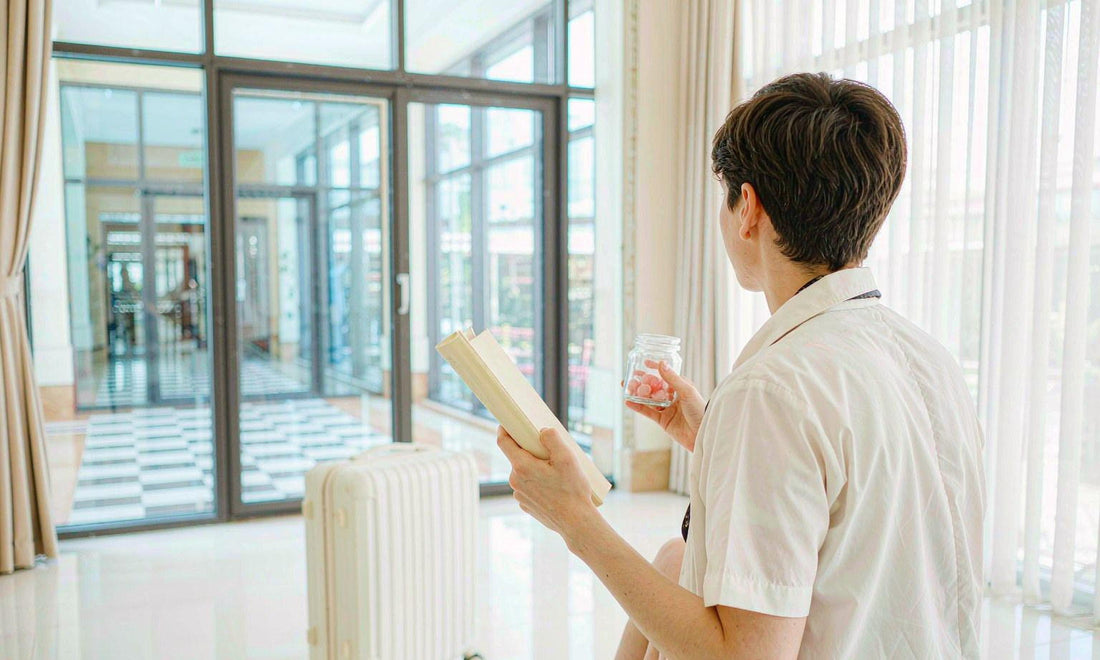 A traveler seen from behind at a bright airport window holding a small gummy jar and a boarding folder
