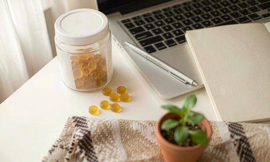 Supplement jar of amber gummies beside a closed laptop and notebook on a bright white desk