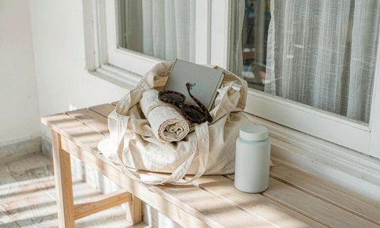 Canvas tote, white supplement bottle and notebook on a light bench by a window