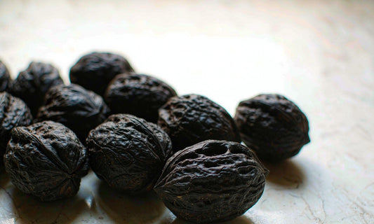 Whole black walnuts in deep textured shells arranged in a row on a pale cream marble surface