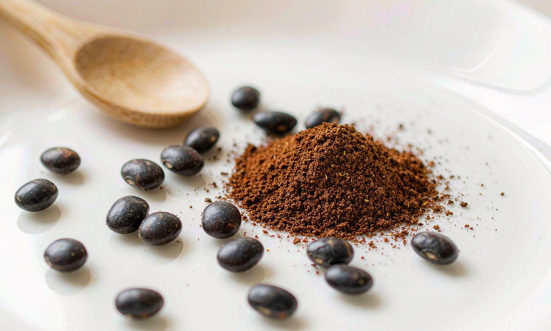 Macro of dark velvet bean seeds and a mound of fine brown powder on white ceramic with a wooden spoon